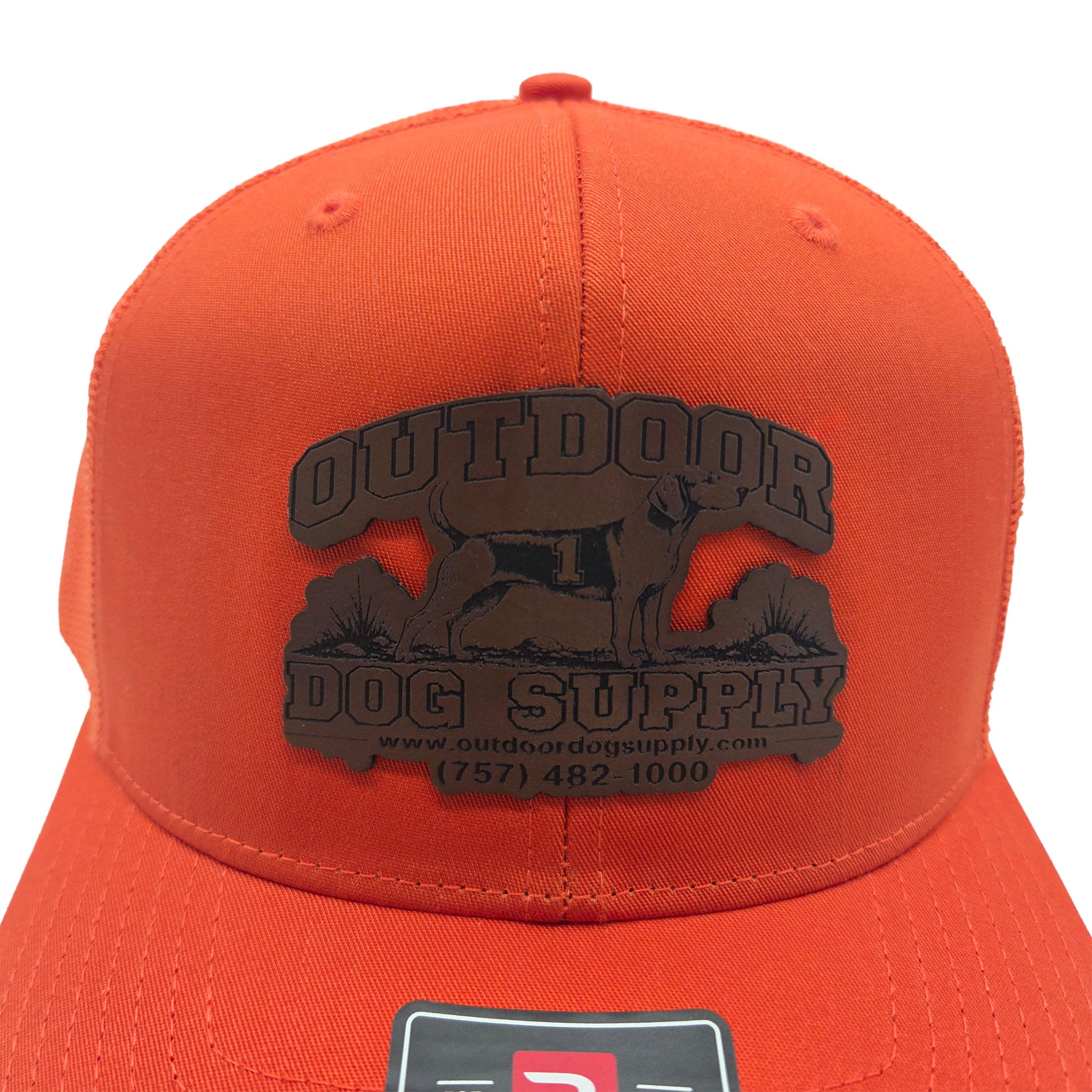 close up of the leather patch that reads "Outdoor Dog Supply www.outdoordogsupply.com (757) 482-1000" on an orange trucker hat